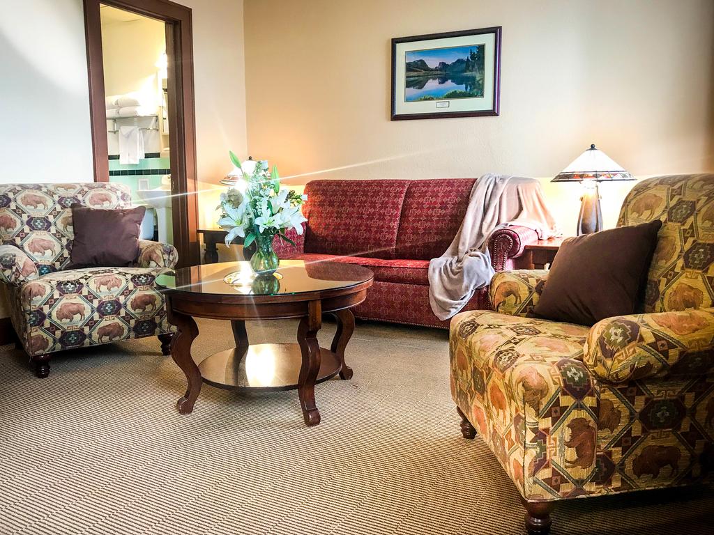 Cozy sitting area featuring patterned armchairs, a red sofa, a glass-top coffee table, and fresh flowers, creating an inviting atmosphere.