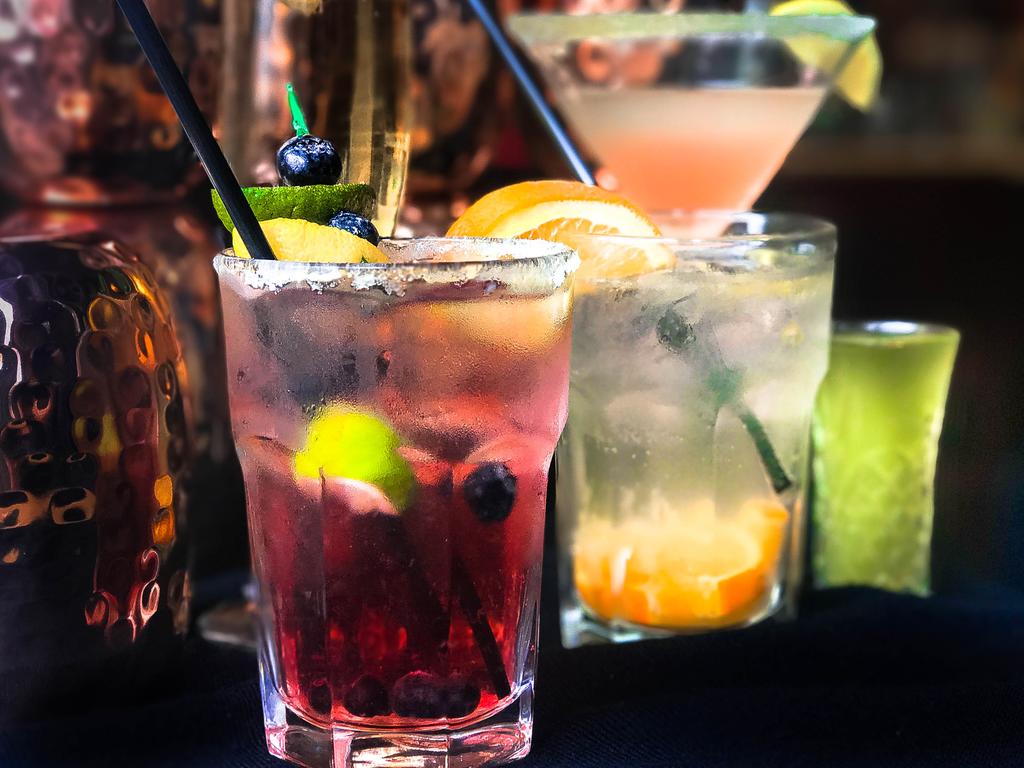 Colorful cocktails in clear glasses garnished with fresh fruits, served against a dark background, showcasing a vibrant drink selection for a festive atmosphere.