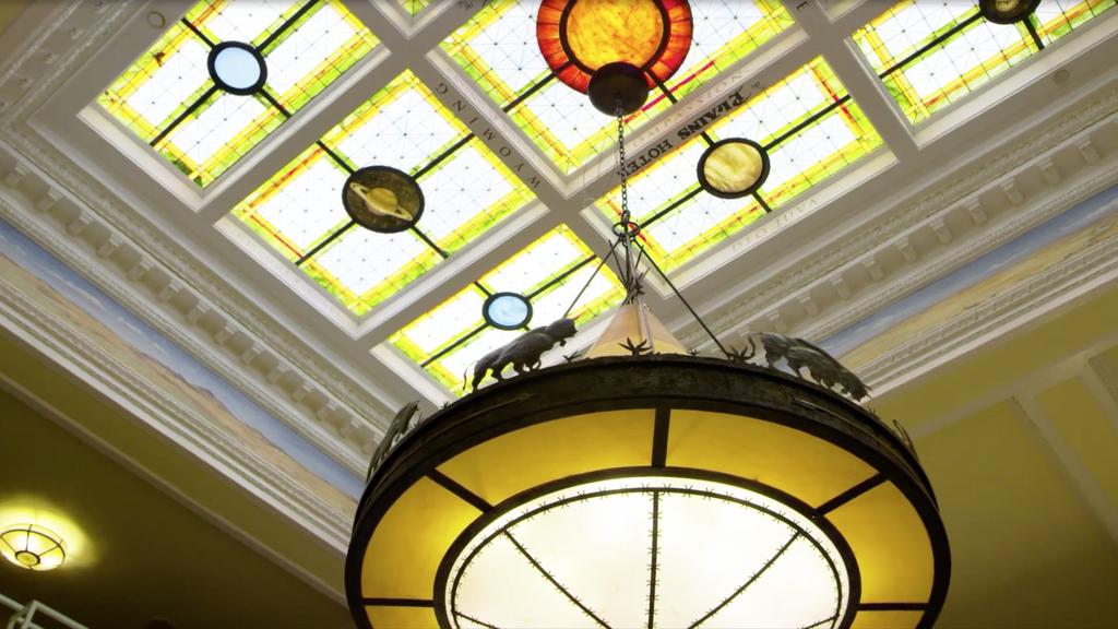Victorian chandelier with animal motifs hangs beneath a colorful stained glass ceiling, showcasing architectural elegance in a historic building.