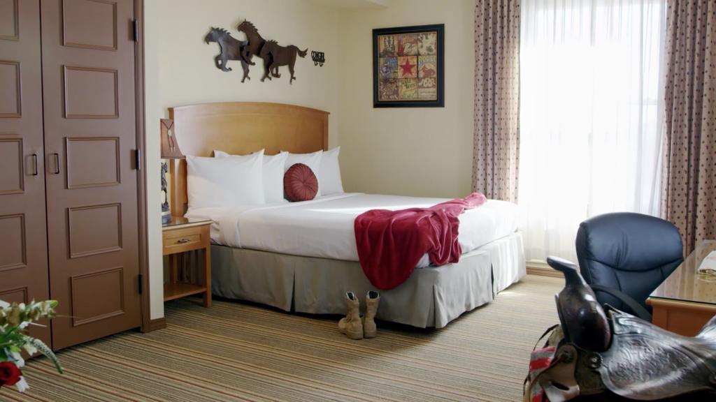 Cozy bedroom featuring a queen bed with white linens, a red throw, and Western-themed decor, including horse wall art and a saddle chair.